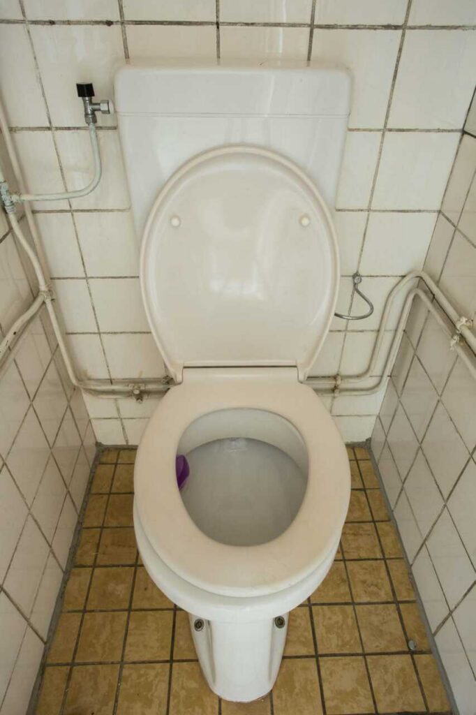 White toilet with open lid in a small tiled bathroom corner.