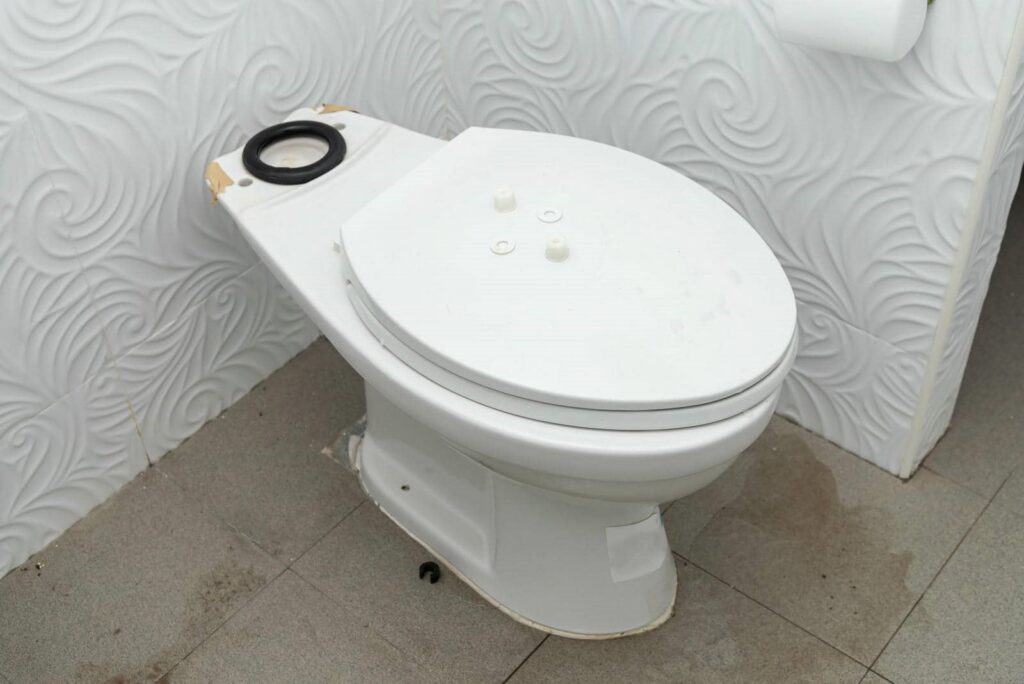 White toilet bowl without a tank installed, placed on a tiled floor with textured white walls.